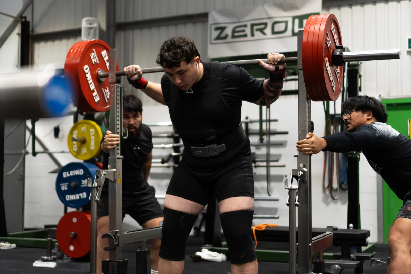 A lifter walking out a heavy squat with spotters either side at ZeroW Wales