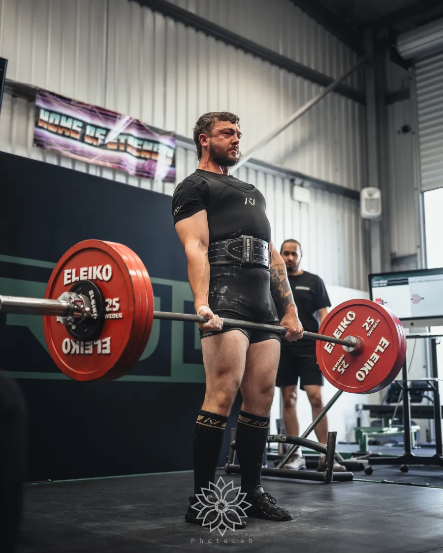 A lifter locking out a deadlift in front of the ZeroW backdrop