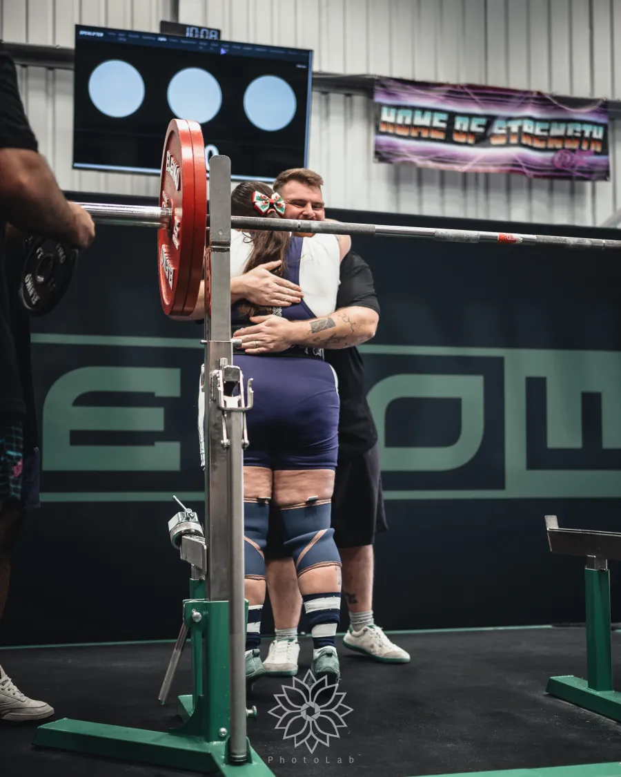 Two lifters hugging at the squat rack after an attempt